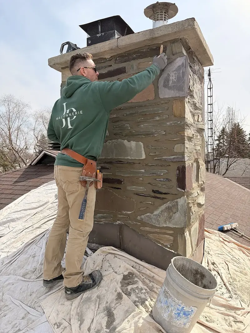 Jean-François, copropriétaire de Maçonnerie JP inc., refait les joints d'une cheminée en pierre sur un toit protégé par des bâches